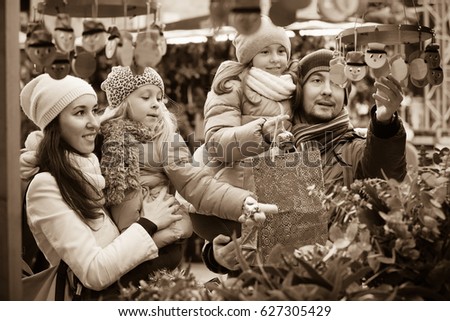 Happy smiling family of four buying Caga Tio at Christmas market. Focus on woman and ittle girl
