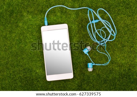 White smart phone and blue earphones on green grass background