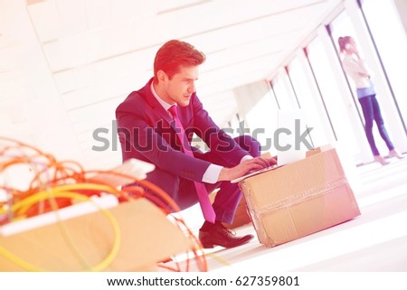 Young businessman crouching while using laptop on cardboard box in new office