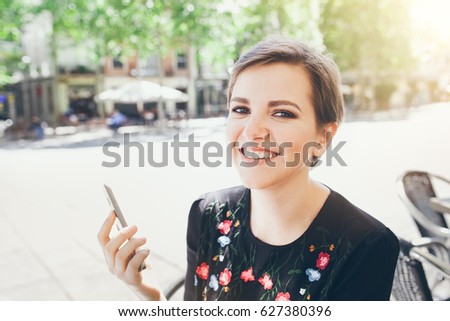 Close-up portrait of attractive young Caucasian woman talking on mobile phone at outdoor cafe. Girl talking by mobile phone, smiling. Sunny day. Outdoor photo.