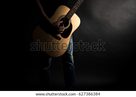 The guitarist in jeans plays an acoustic guitar, on the left side of the frame, on a black background