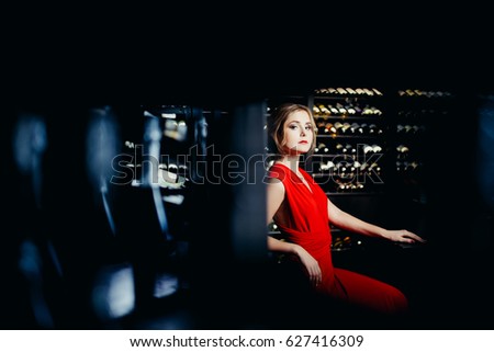 Girl in an evening dress is at a wine tasting in a wine cellar. In the background, racks with bottles. The concept of keeping home wine in a wine cellar.