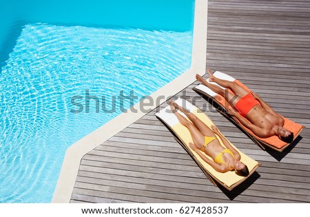 Full length of a young couple resting on sun loungers by swimming pool Royalty-Free Stock Photo #627428537
