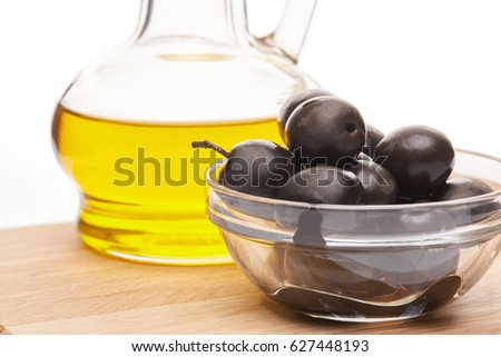 Glass cruet with Extra virgin olive oil, canned black olives in bowl stand on a wooden cutting board on a white background.