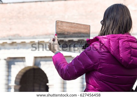 woman is a tourist taking photographs in an European city with her ultra modern transparent smartphone during her travel or trip