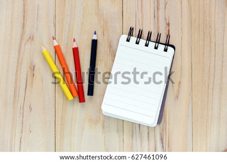 Small note book paper (notepad) for writing information with color pencil on wooden table. view from above