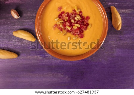 A photo of salmorejo, traditional Spanish cold soup, with bread sticks and crumbs, shot from above on a deep purple wooden texture