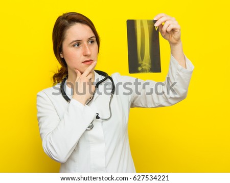 Young female doctor with stethoscope looking at the x-ray picture on yellow background