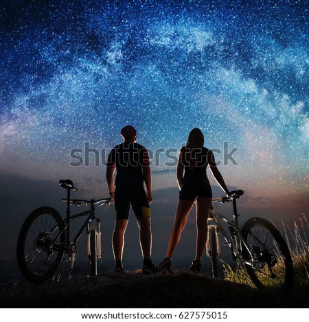 Silhouette couple cyclist enjoying night sky with lots of stars. Bikers with mountain bicycles on the hill at the night
