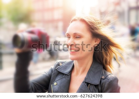 Happy middle aged woman taking pictures while on vacation in a European city. Tourist or traveler having fun. Sunny background. Added blur.