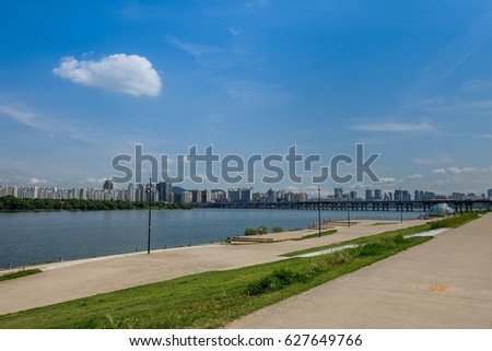The scenery consist of river, blue sky with cloud, green grass and have many building along the river