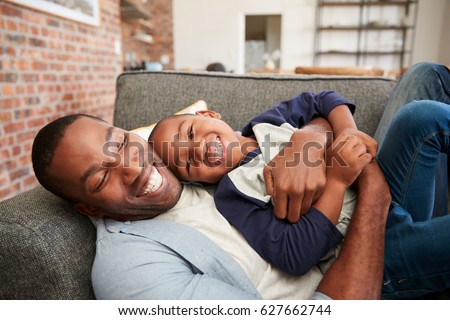 Father And Son Cuddling On Sofa Together Royalty-Free Stock Photo #627662744