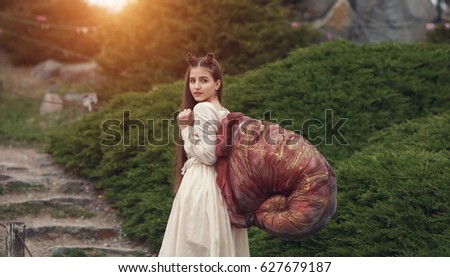 A fabulous snail girl climbs the stone stairs up the rock in the magical forest.
