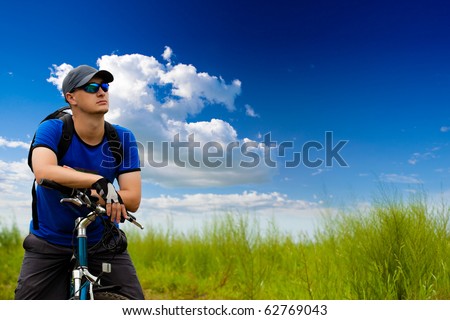 man with bike on green field under blue skies