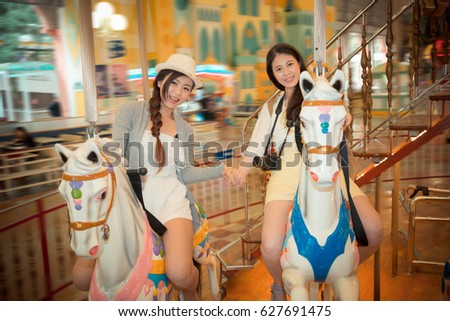 happy sister happy friends on the carousel and hand in hand each other taking the picture together commemorate their summer holiday travel in amusement park. vintage retro film color.