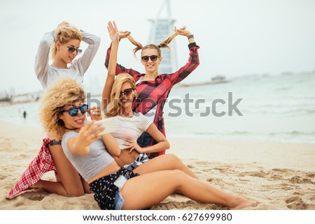 Shot of four young woman having fun on a beach while taking a photo on the mobile phone.
