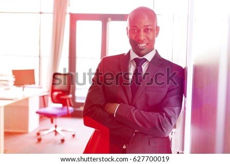 Portrait of smiling young businessman standing arms crossed leaning on cupboard in office