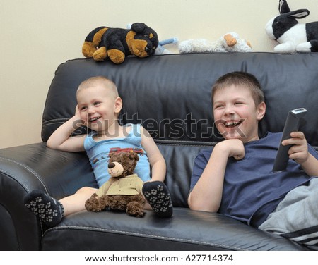 Happy children watching TV on leather couch and having fun together. Two brothers