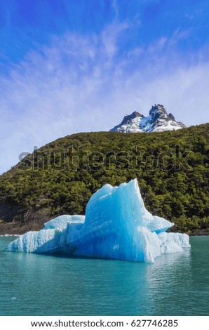 Single big blue iceberg in blue water in the center of the picture, Andes mountain, green hill and blue sky with clouds on the background. Patagonia, Argentina