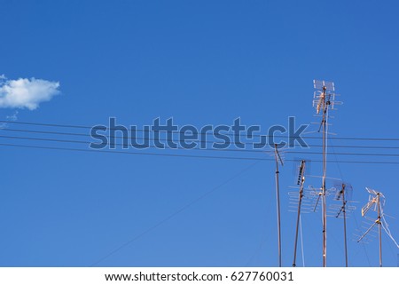 TV antennas against a blue sky with one little white cloud. An abstract concept or metaphor for having a podcast, communication, sending messages, media and cable television.