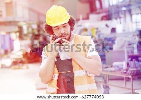 Young manual worker wearing protective clothing while using walkie-talkie in metal industry