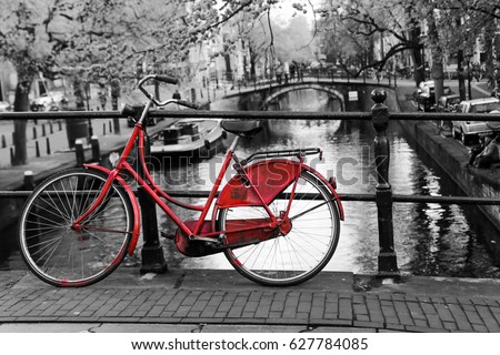 A picture of a lonely red bike on the bridge over the channel in Amsterdam. The background is black and white. 