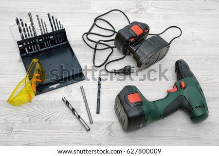 A cordless drill, a spare battery, a set of bits and yellow safety glasses on wooden table background. Handyman. Repairs and DIY. Manual work tools.