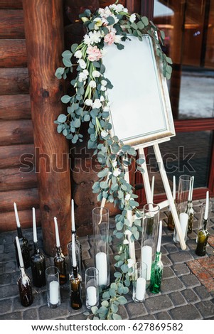Easel with picture decorated with roses stands before the entrance to the house