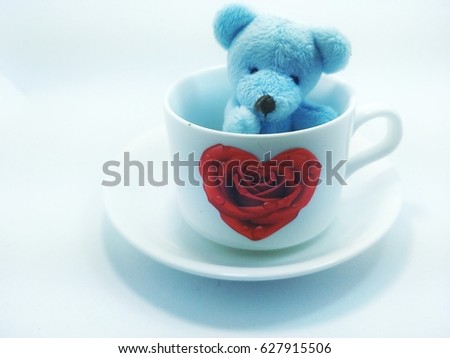 Blue bear in a white cup of rose-shaped roses on a saucer on a white background.