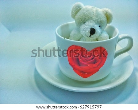 White bear in a white cup of rose-shaped roses on a saucer on a white background.
