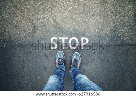 Man standing on grunge asphalt city street with written stop sign on the floor, point of view perspective. Royalty-Free Stock Photo #627916586