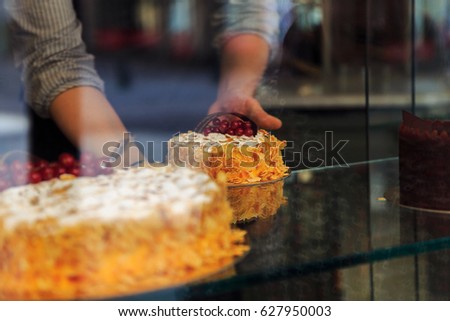 Nice picture of bakery or cafe through the window. A handmade confectionery store or sweet shop window. Selective focus on cakes with fresh berries and almond petals