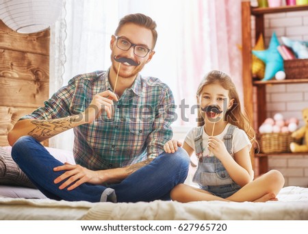 Happy father's day! Dad and his child daughter are playing and having fun together. Beautiful funny girl and daddy have mustaches on sticks. Family holidays and togetherness.