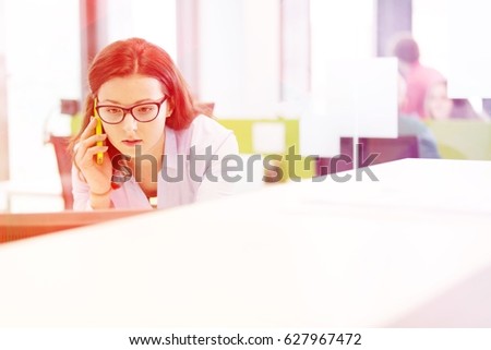 Serious young businesswoman talking on mobile phone in office