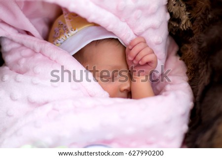 A baby in a hat is sleeping wrapped in a pink blanket