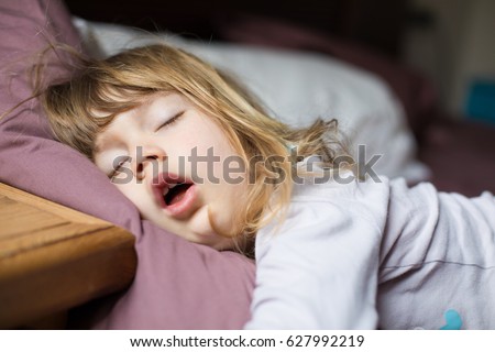 funny face expression with open mouth of blonde caucasian three years old child,  sleeping on  king bed Royalty-Free Stock Photo #627992219