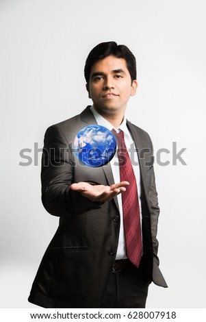 indian/Asian young businessman looking at a floating blue globe or earth model over right palm  while wearing complete corporate dress or attire like suit and tie, isolated over white background