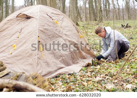 Young man putting a tent in the woods