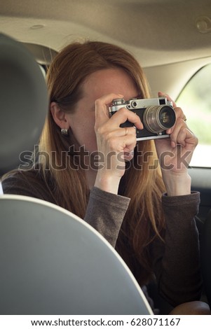 Girl with retro camera taking pictures at the car. Photo taken through glass
