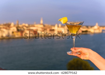 Yellow cocktail in the hand of a girl on the terrace of a building. In the background the city of Venice
