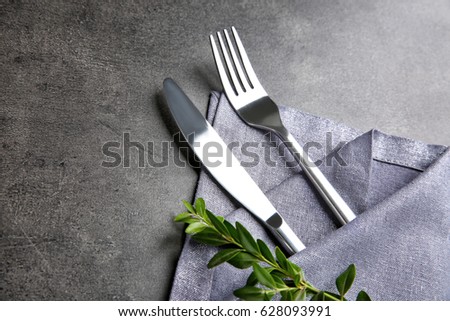 Table setting with silver cutlery in napkin on grunge background