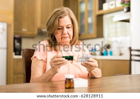 Good looking senior adult woman looking at her pills' expiration date sitting in the kitchen  Royalty-Free Stock Photo #628128911
