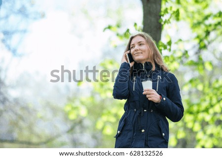 A girl is walking in the morning in a park with a smartphone and coffee