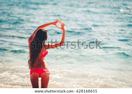 Girl in swim wear on tropical exotic beach making heart symbol by hands. Vintage toned image. Stylish toned picture.