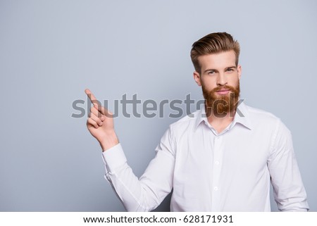 Portrait of serious confident bearded man pointing with fingers on copy space