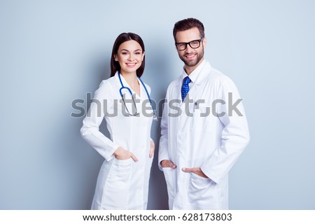 Two best smart professional smiling doctors workers in white coats holding their hands in pockets and together standing against gray background Royalty-Free Stock Photo #628173803