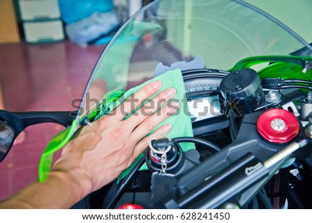 Hand cleaning the motorcycle with green microfiber cloth