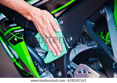 Hand cleaning the motorcycle with green microfiber cloth