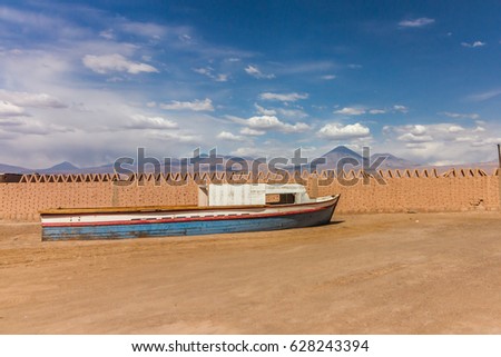 An abandoned boat in the desert with the majestic licancabur volcano in the background in a beautiful blue sky and clouds - San Pedro do Atacama - Chile
