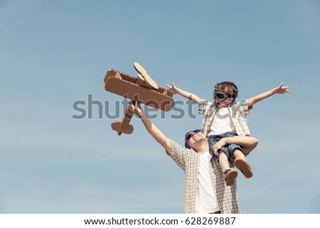 Father and son playing with cardboard toy airplane in the park at the day time. Concept of friendly family. People having fun outdoors. Picture made on the background of blue sky.